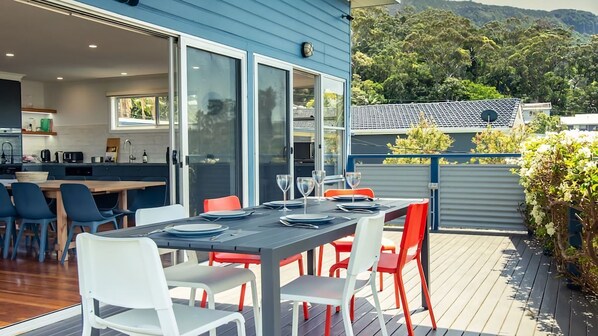 An outdoor dining area with a table set for four, surrounded by chairs, and a view of a mountain and trees in the background. - Oceanview Escape One Hour from Sydney (Wombarra)