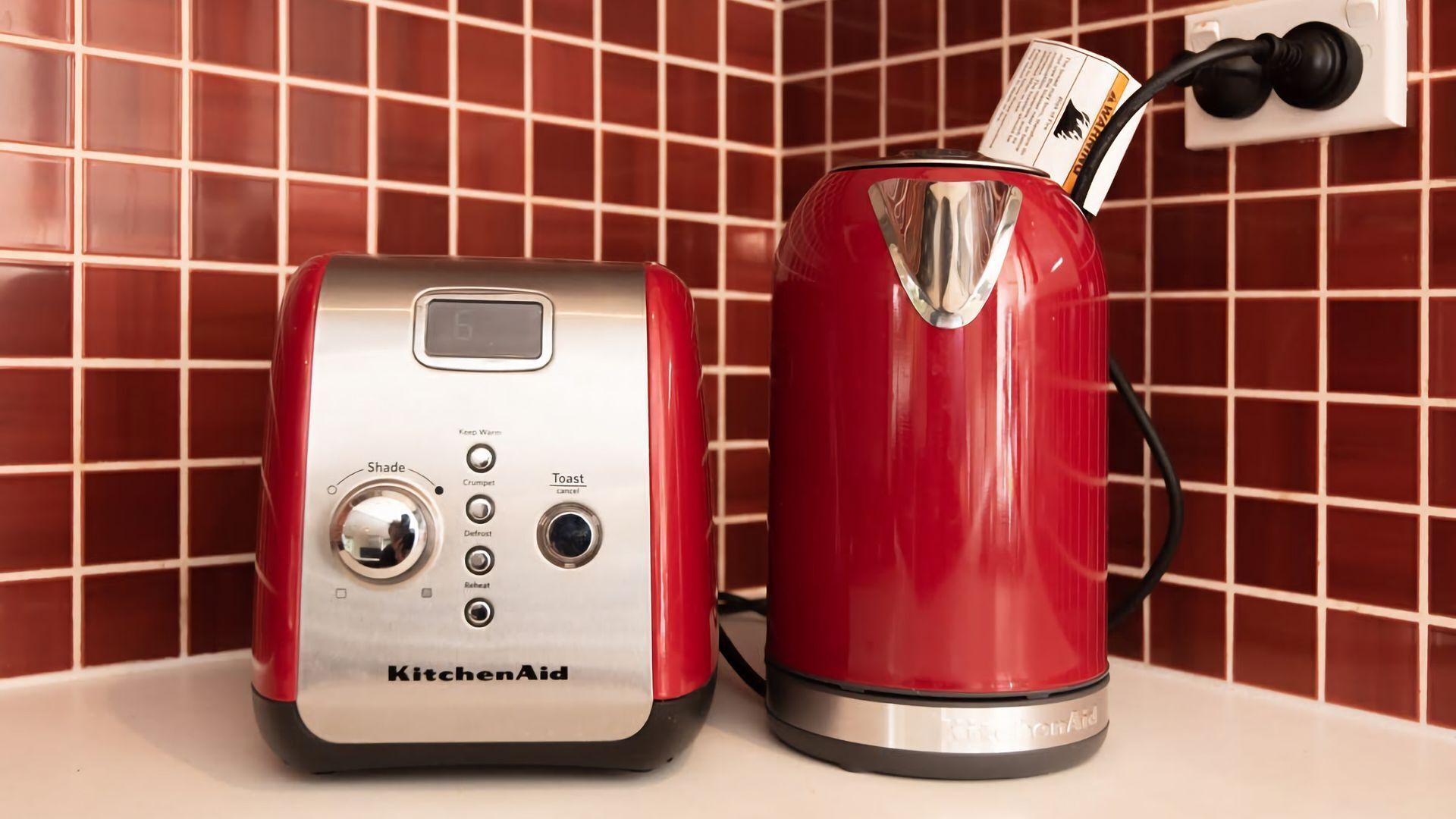 En KitchenAid-toaster og elkedel på en bordplade med flisebeklædt bagvæg.