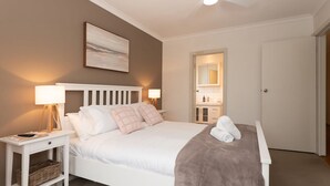 Une chambre à coucher avec un lit, des tables de chevet, une lampe, un tableau, un miroir et une porte.
