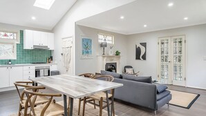 A modern kitchen with white cabinets, a marble countertop, and a dining area with a wooden table and chairs. - Katoomba Cottage Escape Near the Three Sisters (Katoomba)