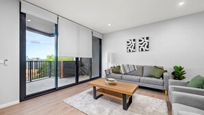 Un salon moderne avec un canapé gris, une table basse en bois et une vue sur un balcon.