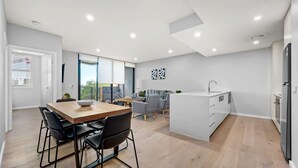 Une cuisine moderne dotée d’un îlot central, un coin repas avec une table et des chaises en bois, et un espace de vie comprenant un canapé et un téléviseur.