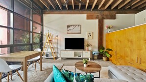 A modern living room with a wooden ceiling, a large TV, a sofa, a coffee table, and a cabinet. - Brick & Beam New York Style Loft in Chippendale (Chippendale)