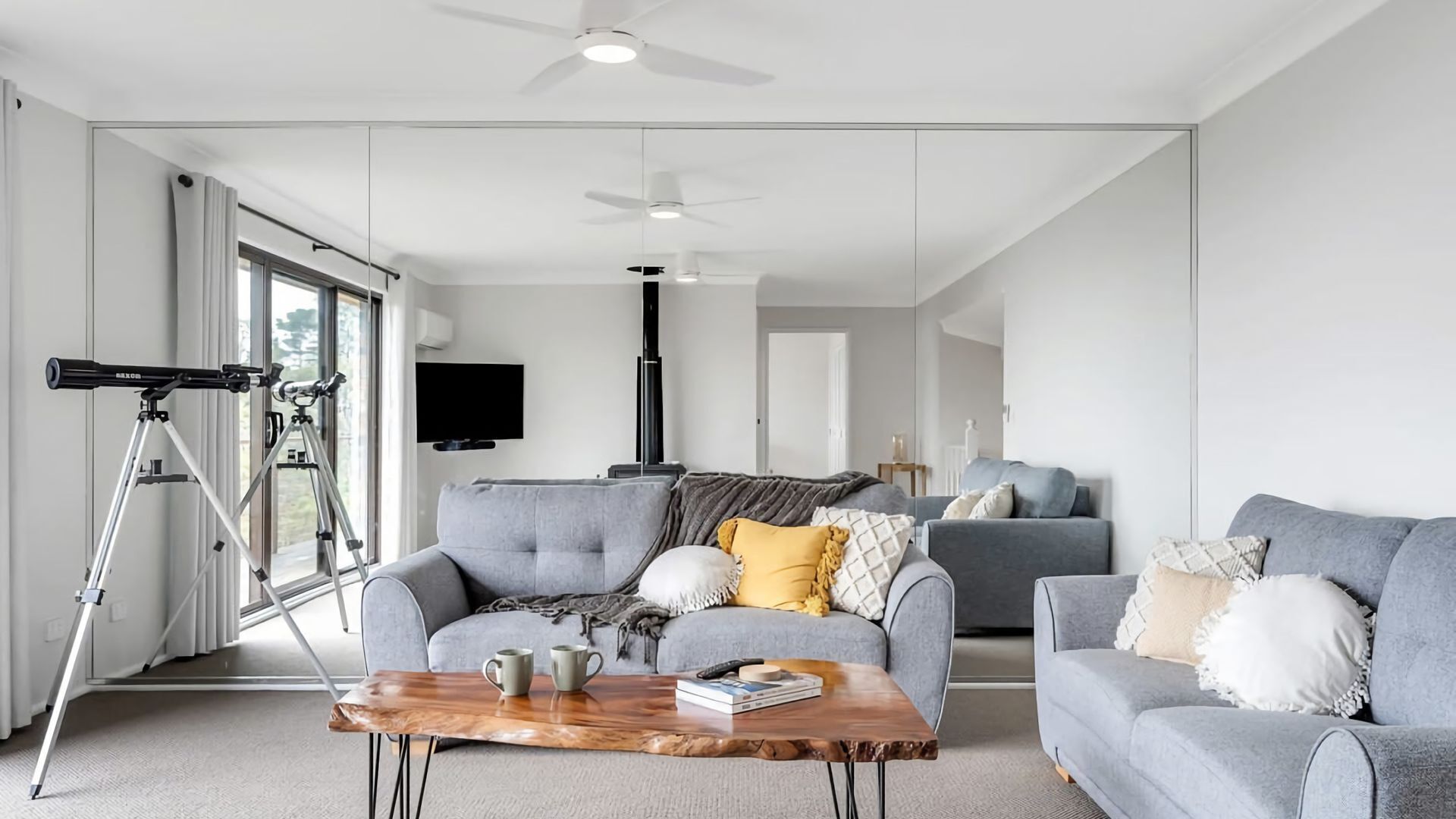 A modern living room with a grey sofa, a coffee table, and a telescope on a tripod.