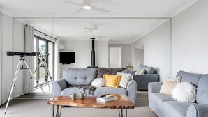 A modern living room with a grey sofa, a coffee table, and a telescope on a tripod. - Mountain View Hideout with Stargazing Telescope (Wentworth Falls)