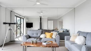 A modern living room with a grey sofa, a coffee table, and a telescope on a tripod.