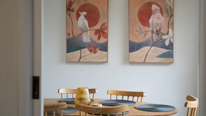 A dining area with a wooden table, blue cushions, and a yellow vase. Two paintings of birds are on the wall. - Mountain View Hideout with Stargazing Telescope (Wentworth Falls)