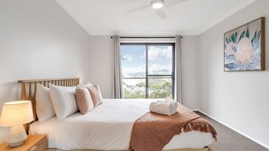 A bedroom with a large window, a bed with a wooden headboard, a bedside lamp, and a painting on the wall. - Mountain View Hideout with Stargazing Telescope (Wentworth Falls)