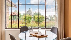 A dining area with a round glass table, two chairs, and a view of a garden through large windows. - Mountain View Hideout with Stargazing Telescope (Wentworth Falls)
