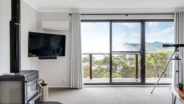 A modern living room with a TV, fireplace, and balcony with a scenic view. - Mountain View Hideout with Stargazing Telescope (Wentworth Falls)