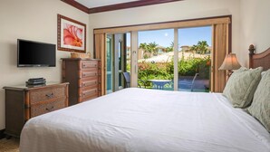 A hotel room with a large bed, a television, a dresser, and a view of a pool and palm trees.