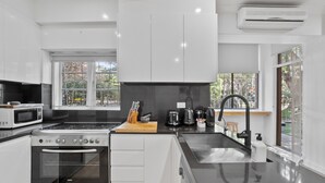 A modern kitchen with white cabinets, a Bosch oven, a microwave, a sink, and a window with a view of trees. - Pet-Friendly Home Just Minutes from Bondi Beach (Bellevue Hill)
