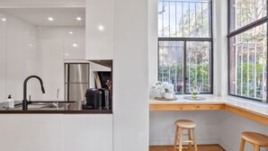 A modern kitchen with white cabinets, stainless steel appliances, and a black faucet. There is a window with a view of trees and a wooden bench. - Pet-Friendly Home Just Minutes from Bondi Beach (Bellevue Hill)