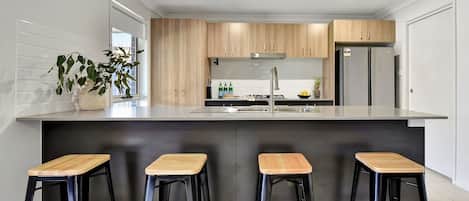 Eine moderne Küche mit Holzausstattung, einem Edelstahlspülbecken und einer Bar mit Hockern.