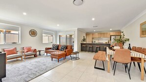 Amplia sala de estar con un juego de sofás, una mesa de comedor con sillas, una zona de cocina y un ventanal que proporciona luz natural.