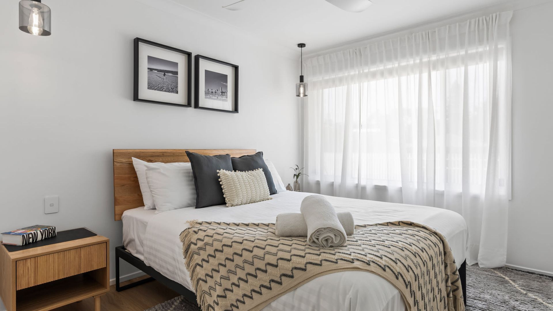 A bedroom with a bed, a nightstand, a lamp, and two framed pictures on the wall.