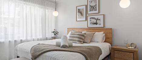 Une chambre à coucher bien rangée, avec un lit, des tables de chevet et des œuvres d’art accrochées au mur.