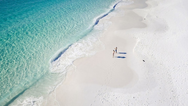 Eine Luftaufnahme eines Strandes mit klarem türkisblauem Wasser und weißem Sand.