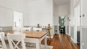 Ein geräumiger Essbereich mit Holztisch und weißen Stühlen, ein kleiner Beistelltisch mit dekorativen Vasen und Blick in ein Schlafzimmer mit Bett und Nachttisch.