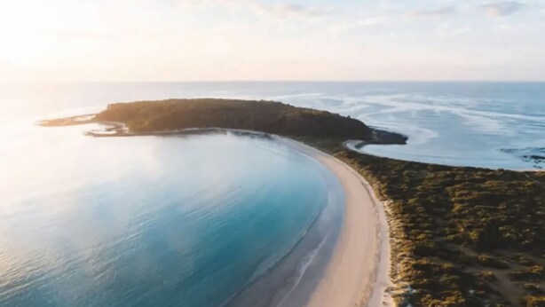 Vista aérea de una zona costera con playa, una pequeña isla y cielo despejado.