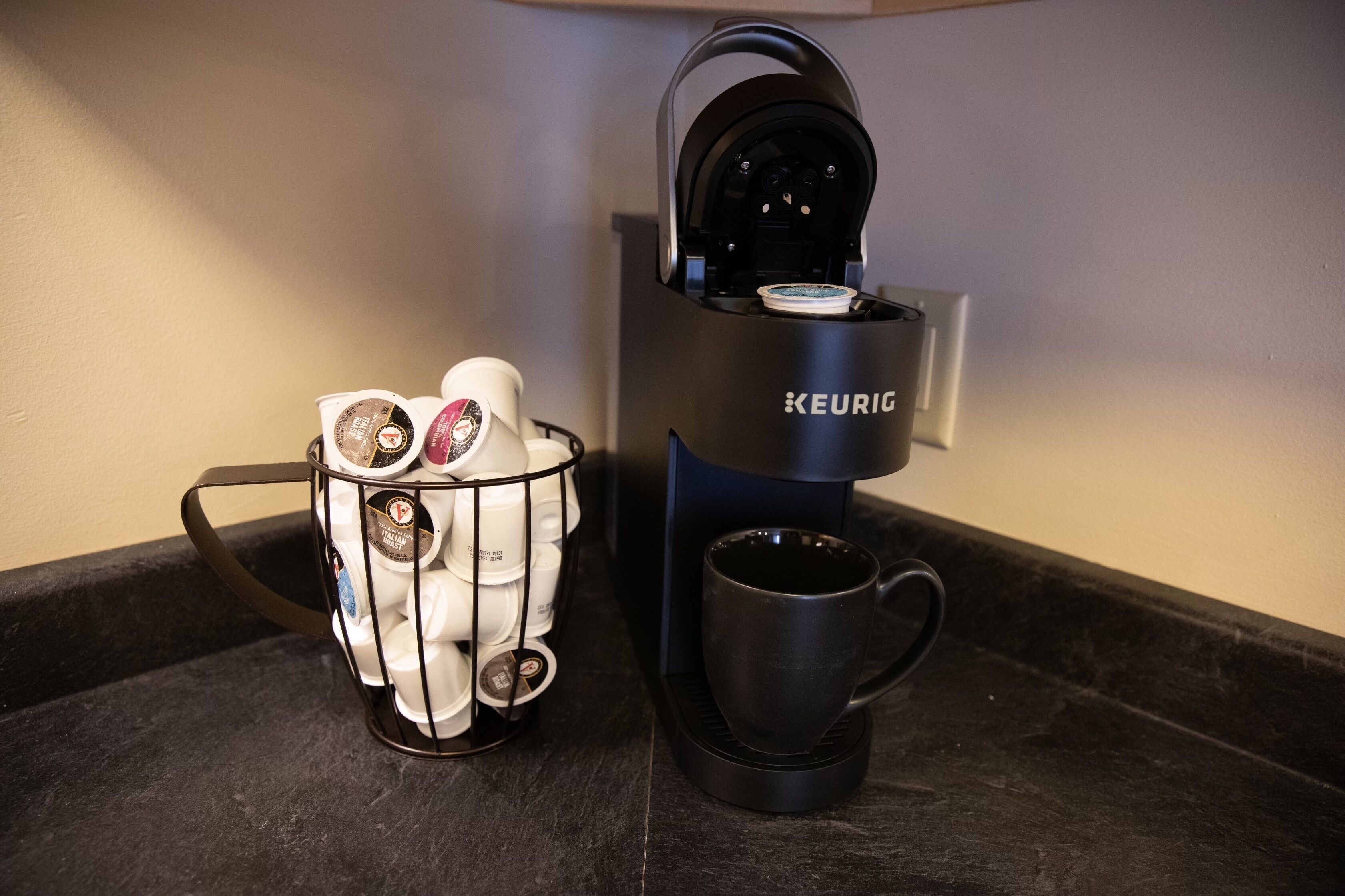 A Keurig coffee machine with a mug and a cup holder containing multiple coffee pods.