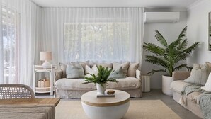 Un salón moderno con un conjunto de sofá, una mesa de centro y un gran ventanal con cortinas translúcidas.