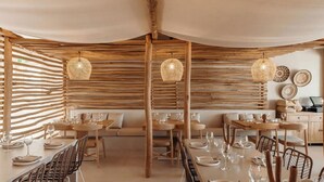 Un restaurante con paredes de listones de madera, lámparas de fibra tejida y diferentes opciones de asientos, incluyendo mesas y sillas.
