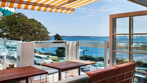 Una terraza con mesas y sillas, con vistas a un cuerpo de agua y una costa lejana.