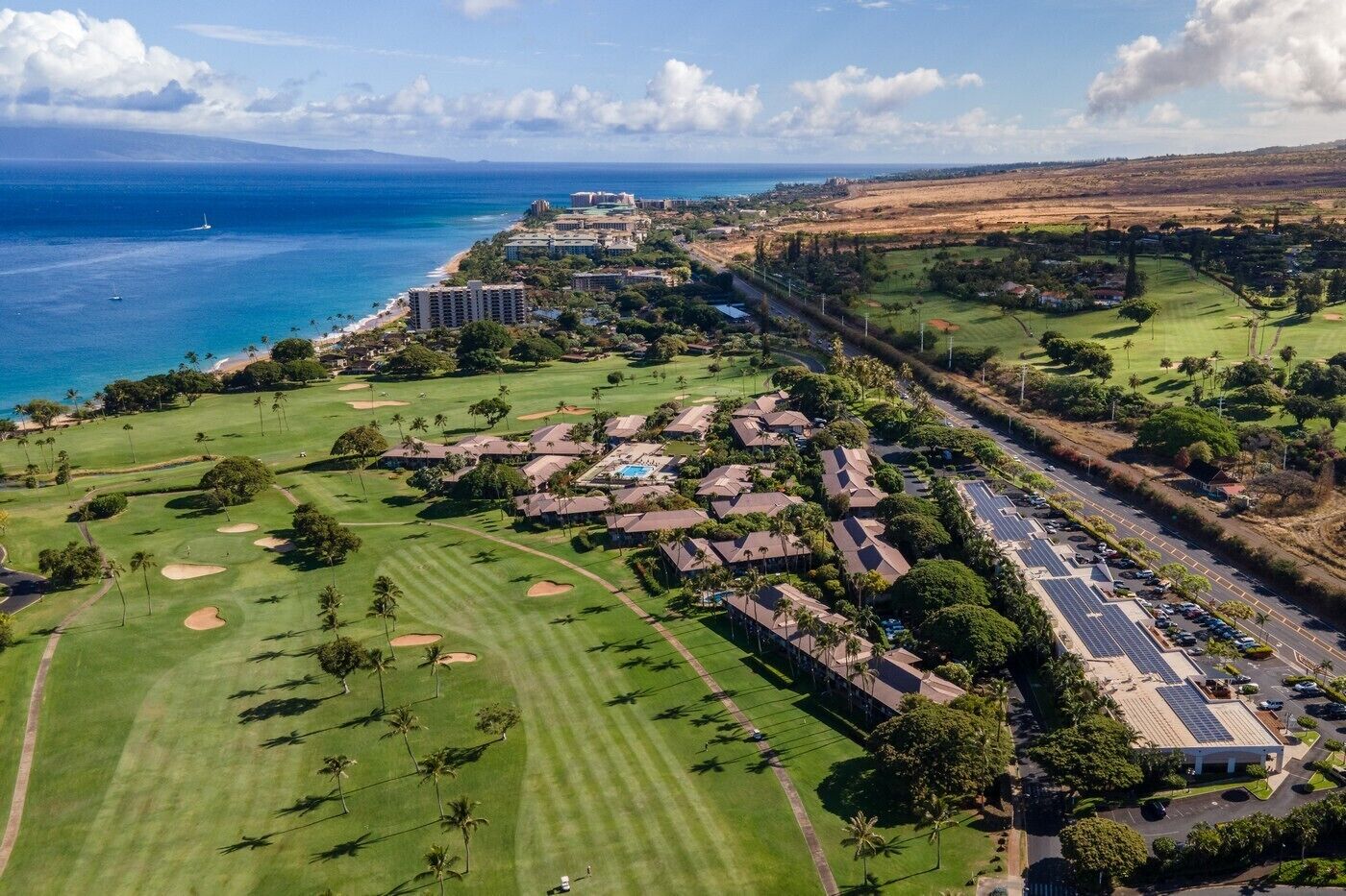 An aerial view of a golf course with a hotel, a road, and a coastline.