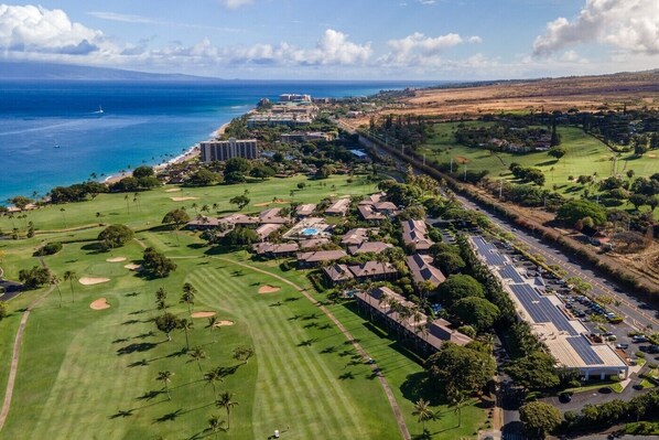An aerial view of a golf course with a hotel, a road, and a coastline.