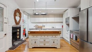 A modern kitchen with white cabinetry, a central island with drawers, a built-in oven, and a stainless steel refrigerator. - The Residence at Leura Falls (Katoomba)