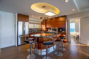 Une cuisine moderne dotée d’un îlot central, d’appareils électroménagers en acier inoxydable et d’un coin bar avec des tabourets.