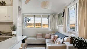 Ein gemütliches Wohnzimmer mit einer Couch, einem kleinen Tisch und Blick auf eine ländliche Landschaft durch große Fenster.