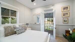 Ein Schlafzimmer mit einem großen Bett, einem Fenster, einer Tür, die auf einen Balkon führt, und gerahmten Bildern an der Wand.