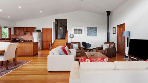 Ein großzügiger Wohnbereich mit einer Couch, einem Couchtisch und Sesseln, eine Küche mit Holzschränken, ein Kamin und ein Fernseher.
