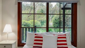 Ein Schlafzimmer mit großem Fenster, einer Nachttischlampe und zwei Kissen mit roten Streifen.