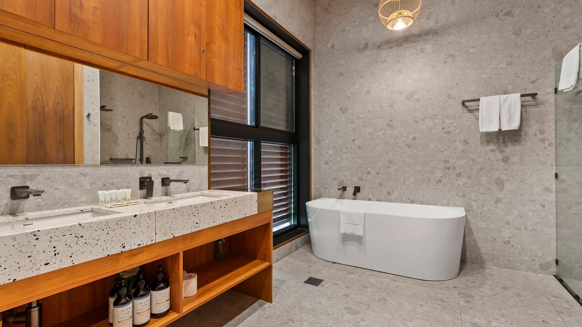 Een moderne badkamer met een vrijstaand bad, een grote spiegel en een houten wastafelmeubel met een getextureerd aanrecht.