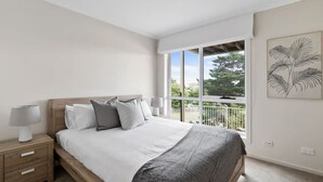 Een slaapkamer met een groot bed, een nachtkastje, een raam met uitzicht en een hangende plant aan de muur.