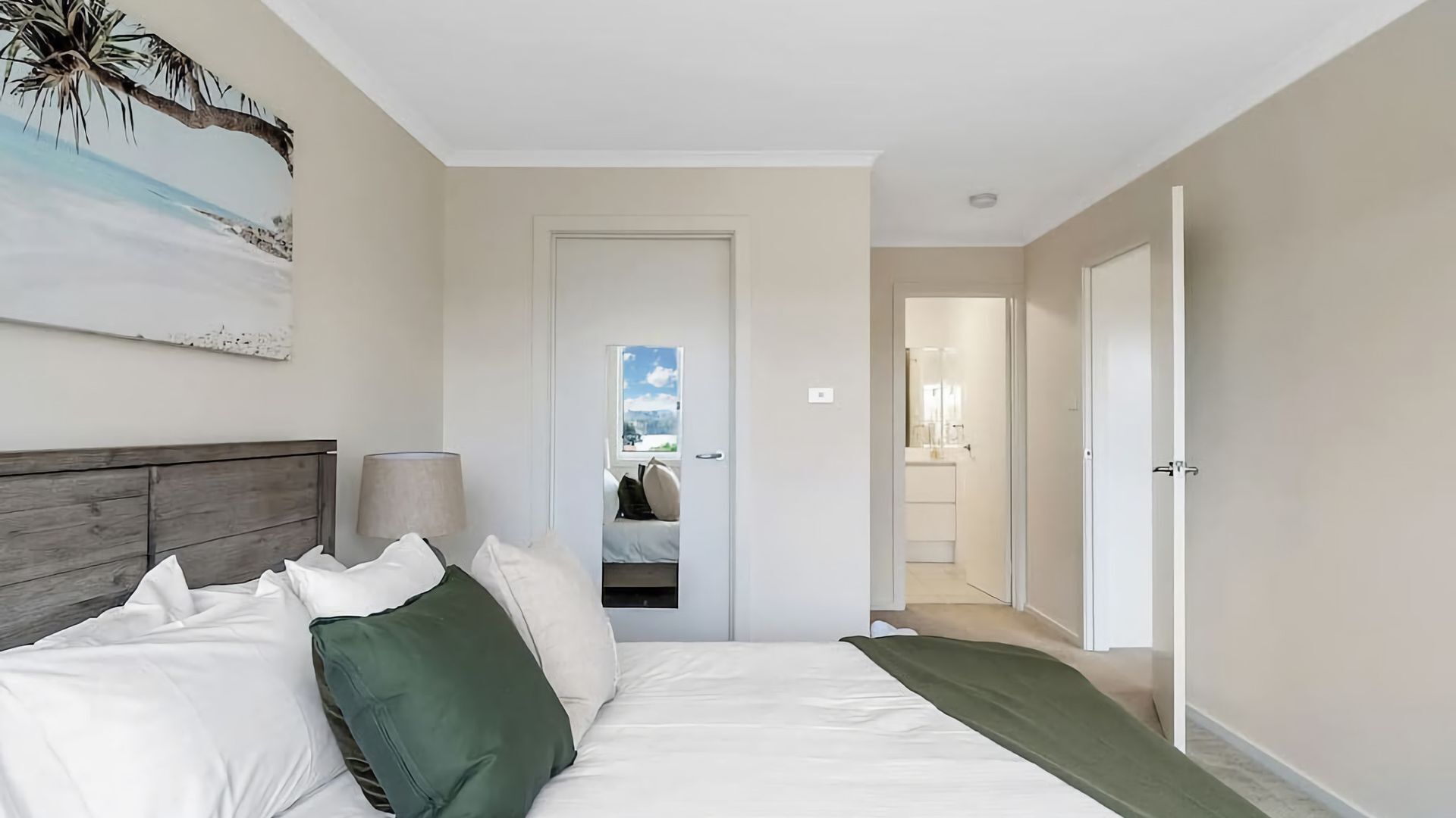A hotel room with a bed, a nightstand, a lamp, a painting, and a view of the bathroom.