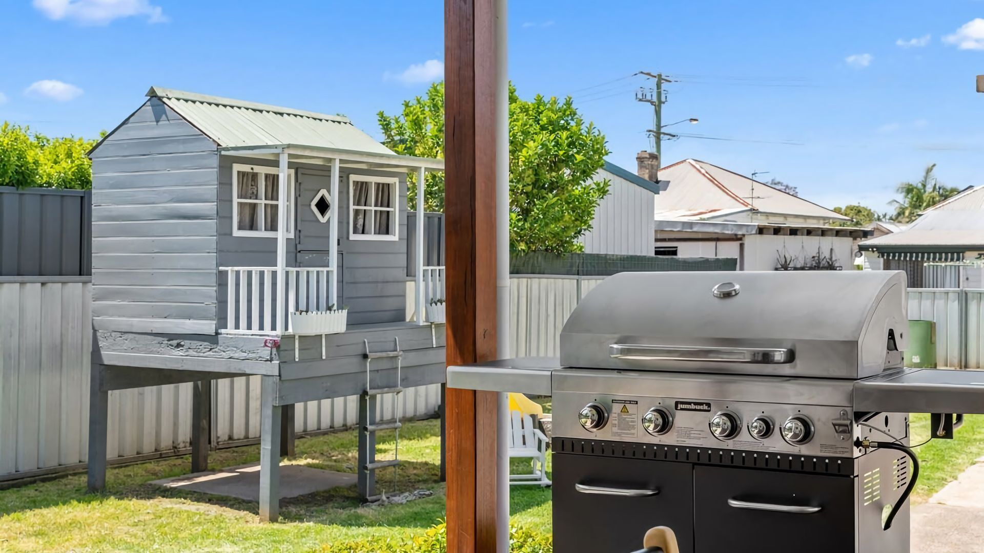 Patio con una parrilla, una casita de juegos de madera y una valla de metal.