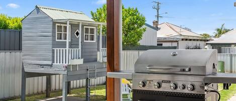 Patio con una parrilla, una casita de juegos de madera y una valla de metal.