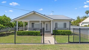A single-story house with a covered porch, a front door, and a small front yard with a black metal fence.