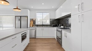 A modern kitchen with white cabinetry, a large window, and a wood floor. - Sip and Soak Up Summer in the Hunter (Cessnock)