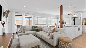 A modern living room with a sectional sofa, ottoman, and a dining area with a table and chairs. - Sip and Soak Up Summer in the Hunter (Cessnock)