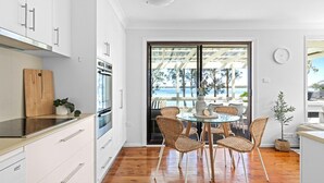 A modern kitchen with white cabinets, stainless steel appliances, and a wooden cutting board. - Sunset Splash Retreat (Budgewoi)