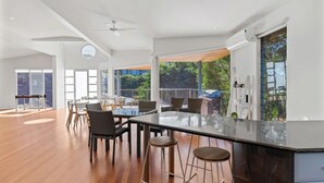 A modern kitchen with a large island, bar stools, and a view of the outdoors. - Bobby's Binburra Beach House (Toowoon Bay)