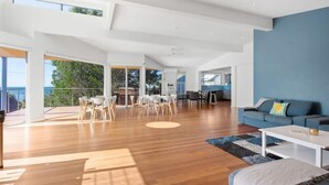A spacious living area with a large dining table, a sofa, and a view of the outdoors. - Bobby's Binburra Beach House (Toowoon Bay)