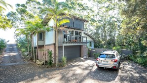 A modern two-story house with a garage, surrounded by lush greenery and a parked car.