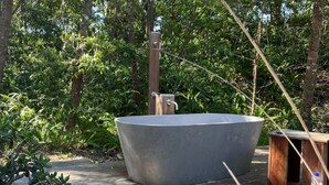 A large outdoor hot tub in a natural setting with a wooden structure nearby.