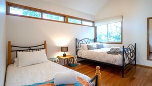 A bedroom with two beds, wooden flooring, and large windows.
